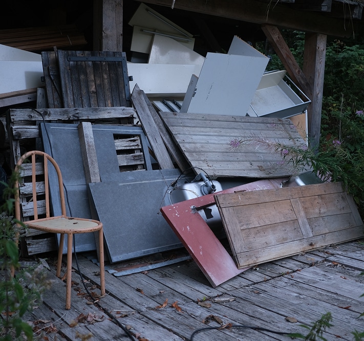 Chaise en métal rouillée à côté d'un tas d'encombrants (bois, éviers, panneaux) sous un abri en bois sombre.
